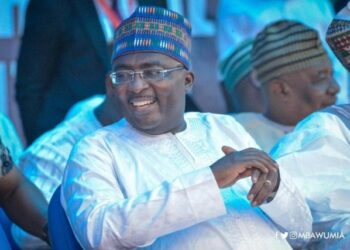 A man with a blue hat and white shirt sitting in a crowd of spectators.